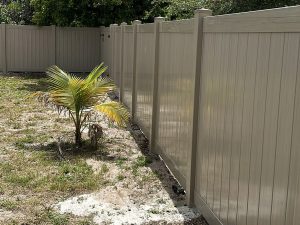 Close-up view of a driftwood-colored PVC privacy fence extending along a residential side yard in Fort Lauderdale, FL.