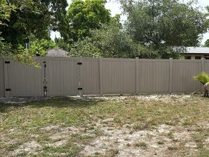 Completed driftwood PVC privacy fence with matching panels and double gates enclosing a residential backyard in Fort Lauderdale, FL.