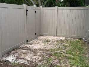 Driftwood PVC privacy fence featuring a matching walk-through gate and black hardware at a residential property in Fort Lauderdale, FL.